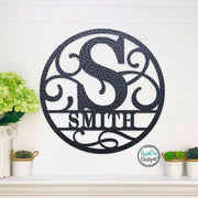 Round metal monogram name sign with decorative scrolling in the background.