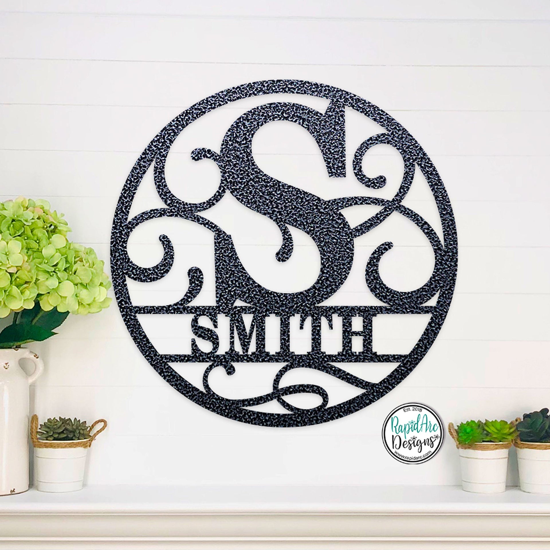 Round metal monogram name sign with decorative scrolling in the background.