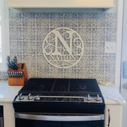 Round metal art wall sign with a full monogram letter with scrolling and a name line underneath the monogram.  The entire design with within the bounds of the circle